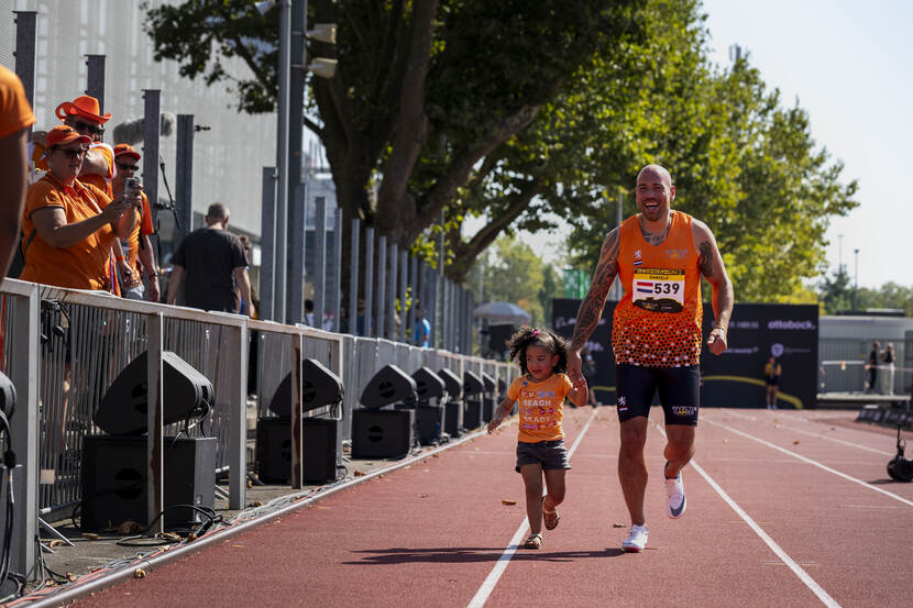 Sporter loopt met zijn kindje aan de hand op de atletiekbaan.