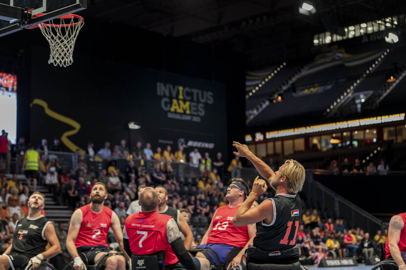 Een rolstoelbasketballer schiet en andere spelers kijken toe.