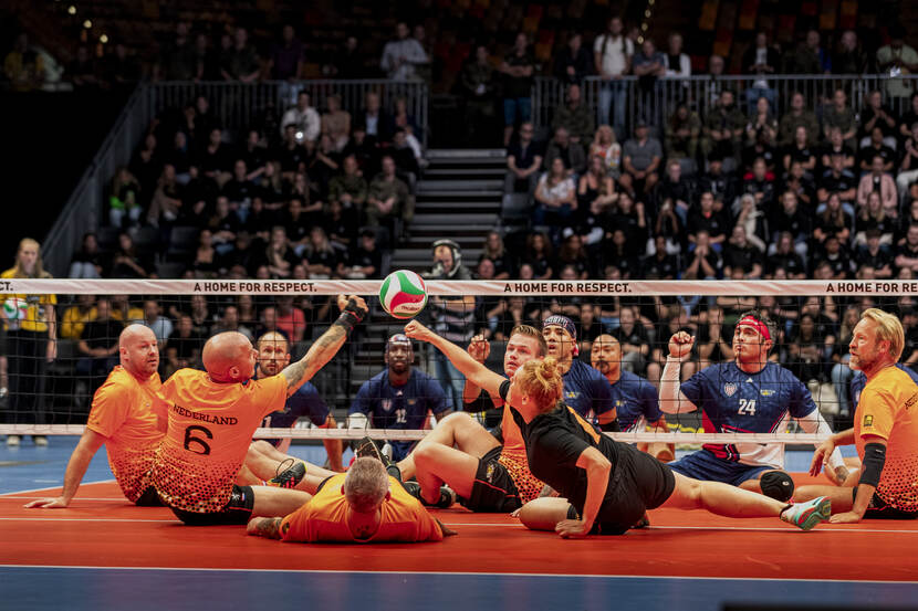 Mannen en vrouwen aan het zitvolleyballen.