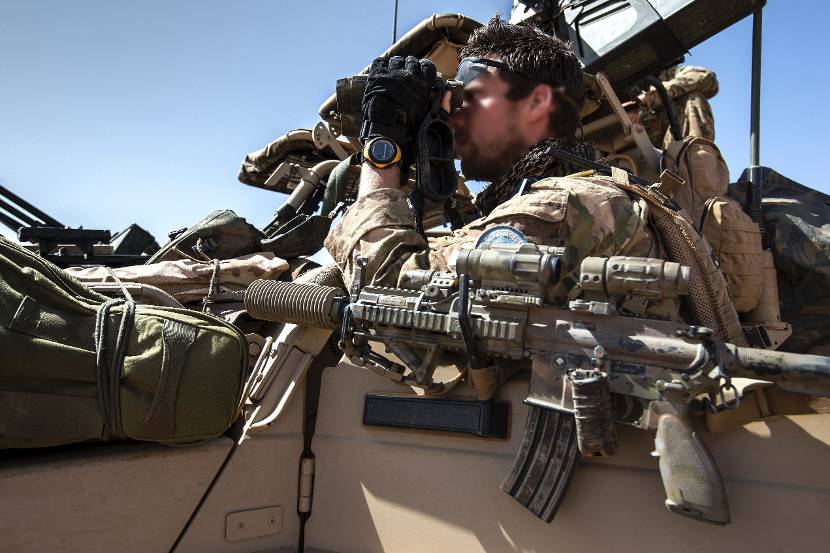 De HK416A5 met geluidsdemper van een commando hangt aan de zijkant van een Mercedes Benz-terreinwagen.