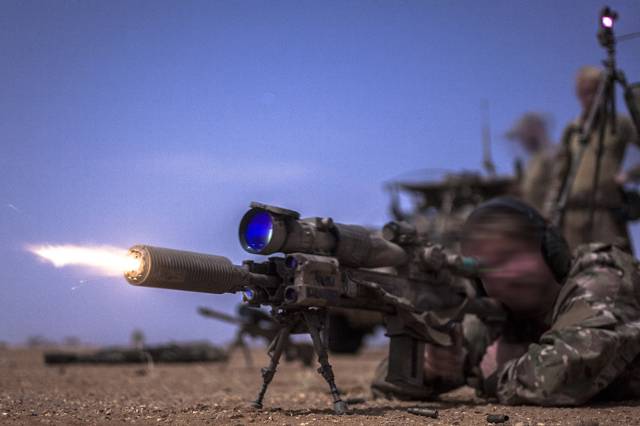 Een commando ligt in de nacht op de grond en schiet met een HK417-scherpschuttersgeweer met geluidsdemper.