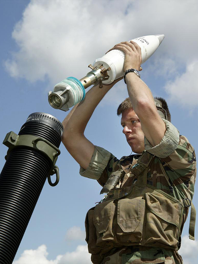 Een militair staat op het punt om een 120mm-rookgranaat af te vuren.