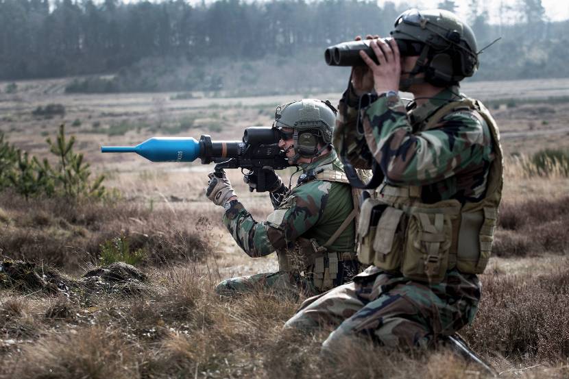 Een marinier staat op het punt om een Panzerfaust 3 af te vuren. Op de voorgrond een militair die door een verrekijker kijkt.