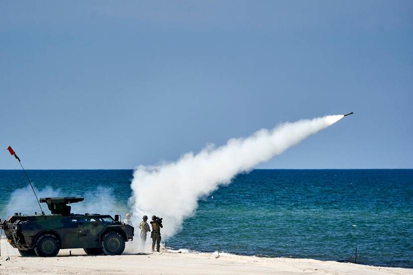 Een militair vuurt een Stinger-raket af. De Stinger hangt over zijn rechter schouder. In de achtergrond de zee.