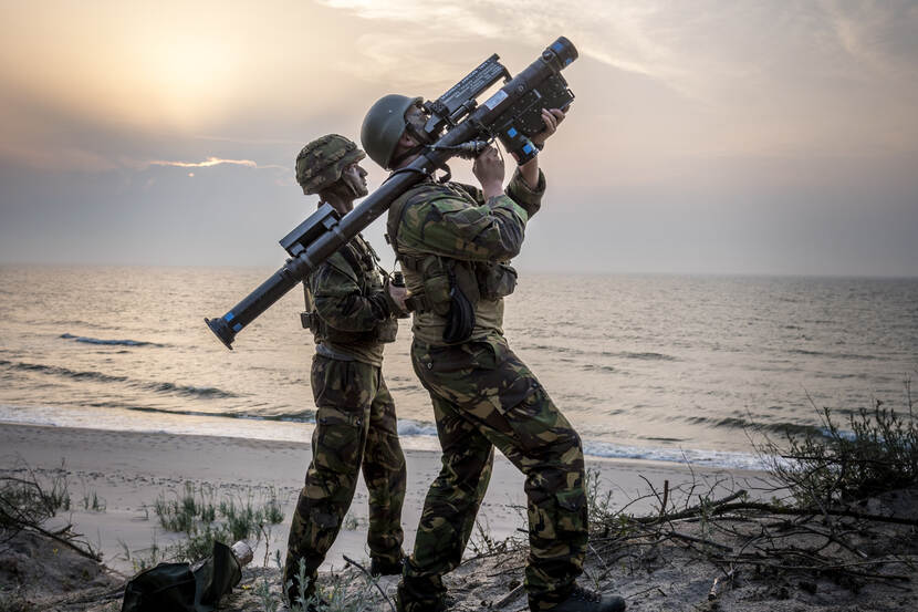 2 militairen staan op een duin. Op de achtergrond het strand en de zee. Een van de militairen heeft een Stinger Manpad op zijn schouder en richt op de lucht.