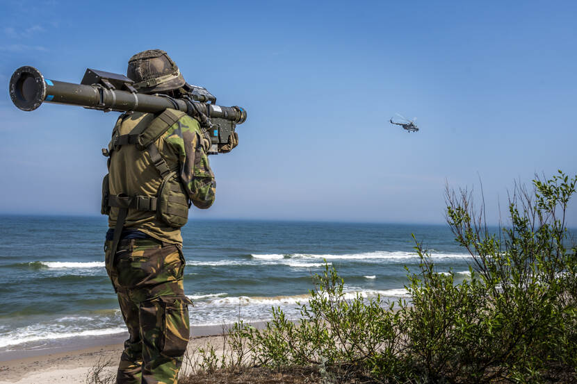 Militair staat op een duin met op zijn schouder een Stinger Manpad. Op de achtergrond de zee. In de verte vliegt een helikopter.