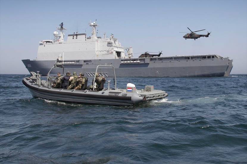 Amfibisch transportschip met 2 transporthelikopters en een snelle motorboot op de voorgrond.
