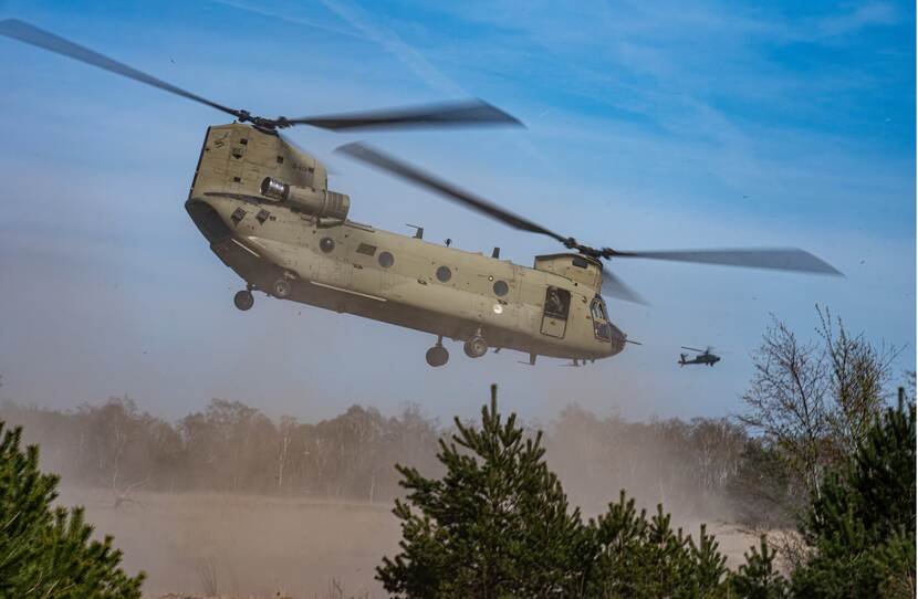 Een Chinook-transporthelikopter stuift zand op bij het opstijgen.