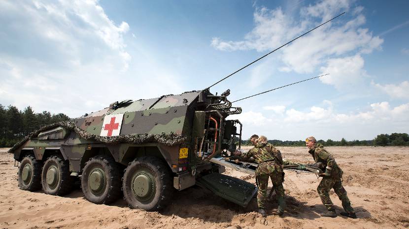 3 militairen duwen een brancard met gewonde een Boxer-ambulance in.