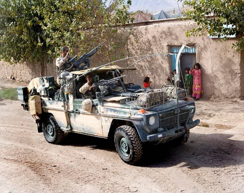 Mercedes-Benz 290GD softtop met zwaaiende bemanning rijdt langs Afghaanse kinderen.