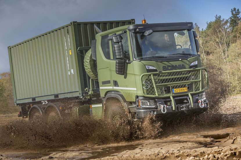 Opspattende modder rond een gloednieuwe, 3-assige Scania Gryphus die op een oefening terrein door plassen rijdt.