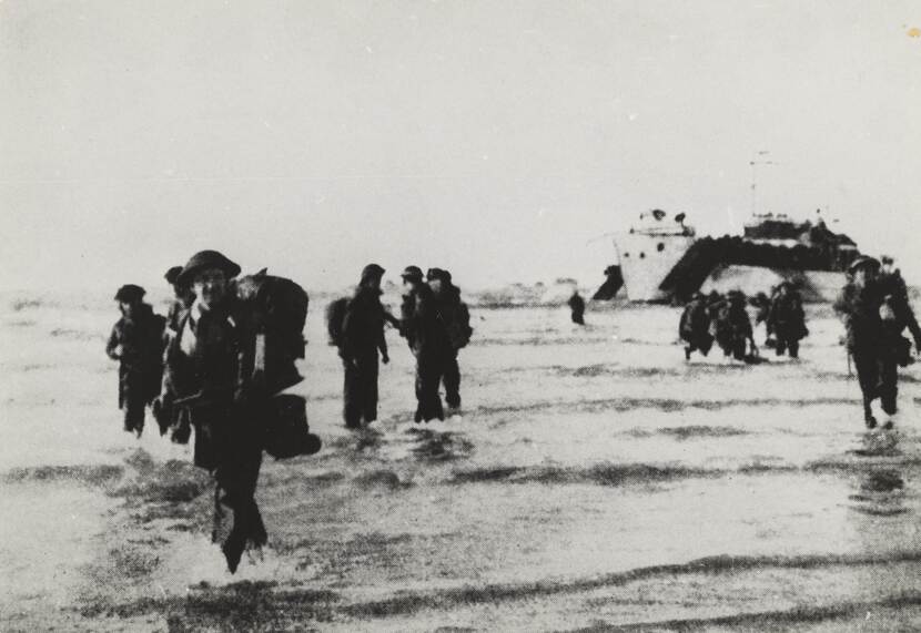Militairen komen door zee aan land in Normandië. In de verte is rechts een landingsvaartuig zichtbaar.