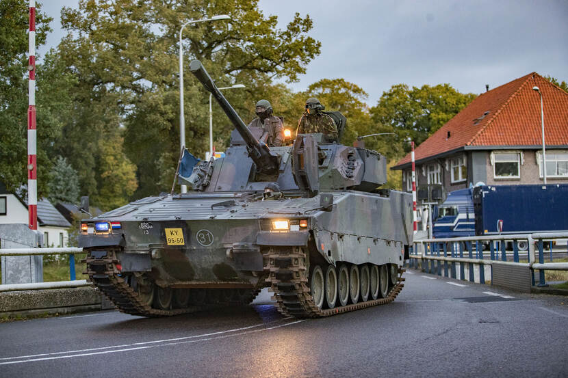 Tank rijdt over een brug, met aan weerskanten huizen.