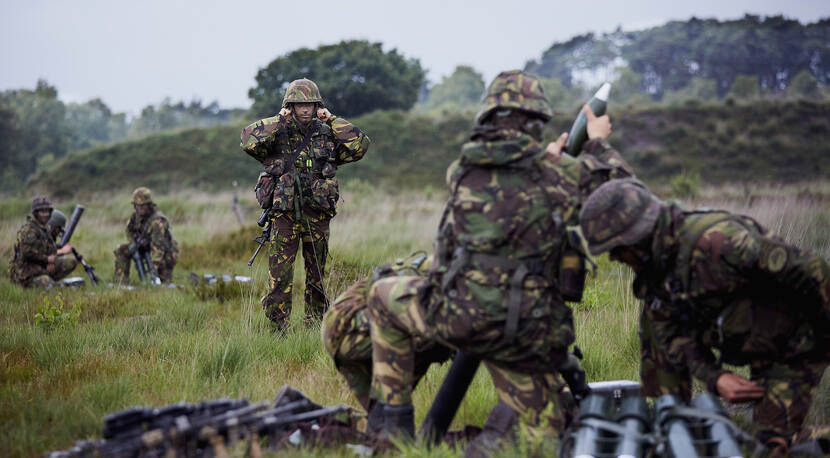 Militairen met gehoorbescherming vuren tijdens oefening, 1 militair houdt vingers in de oren.