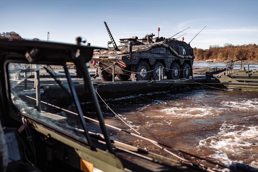 Een militair voertuig wordt met een drijvend platform naar de overkant van een rivier gebracht.