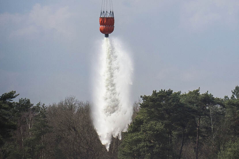 Een bambi bucket lost water boven een bos.