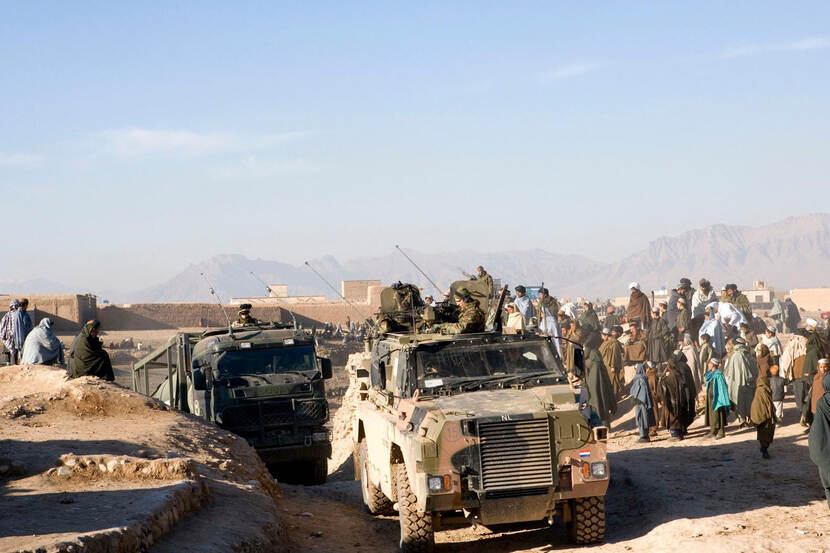 Archief 2007: Militaire voertuigen rijden over zandweg in Tarin Kowt. Mensen kijken toe.