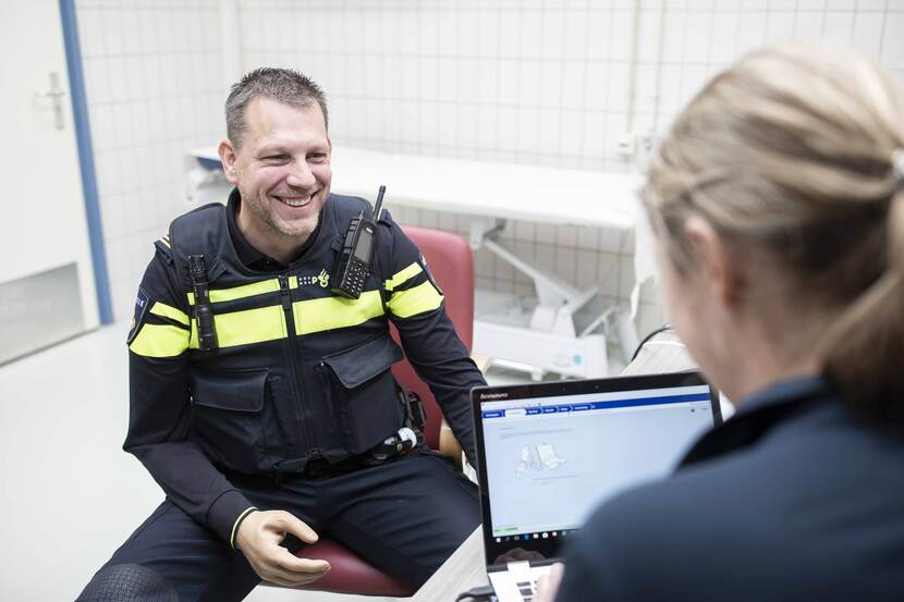 Politieagent met een handprothese zit tegenover een arts met een laptop.