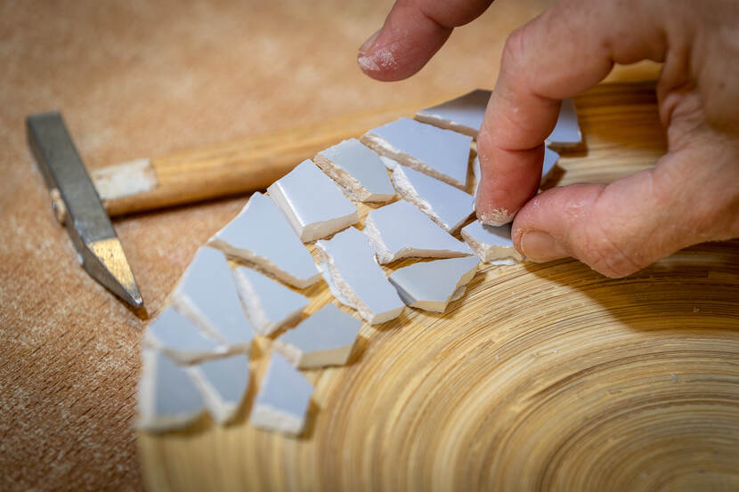 Een man maakt mozaïek  op een bord.