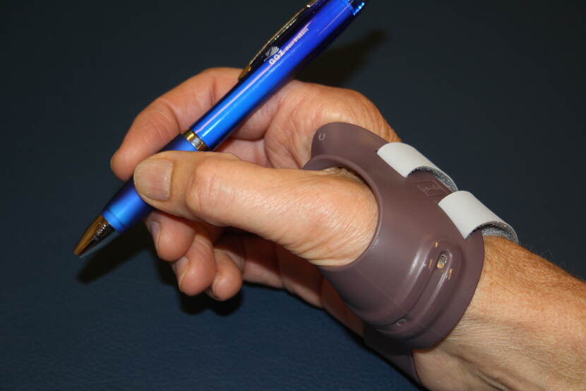 Een hand met een een kunstspalk houdt een pen vast.