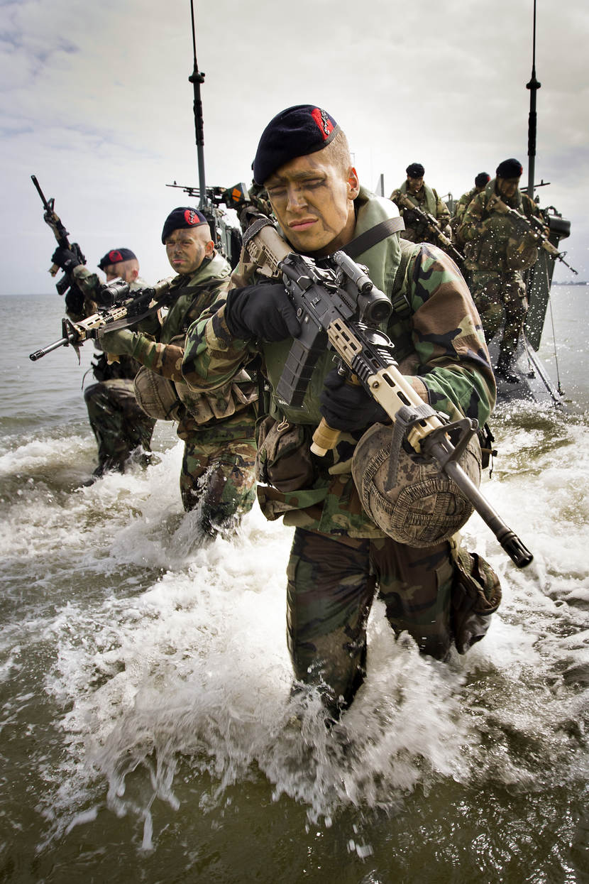 Bewapende mariniers waden door zee.