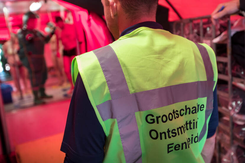 Man met geel hesje. Tekst op achterkant hesje: Grootschalige Ontsmettings Eenheid.