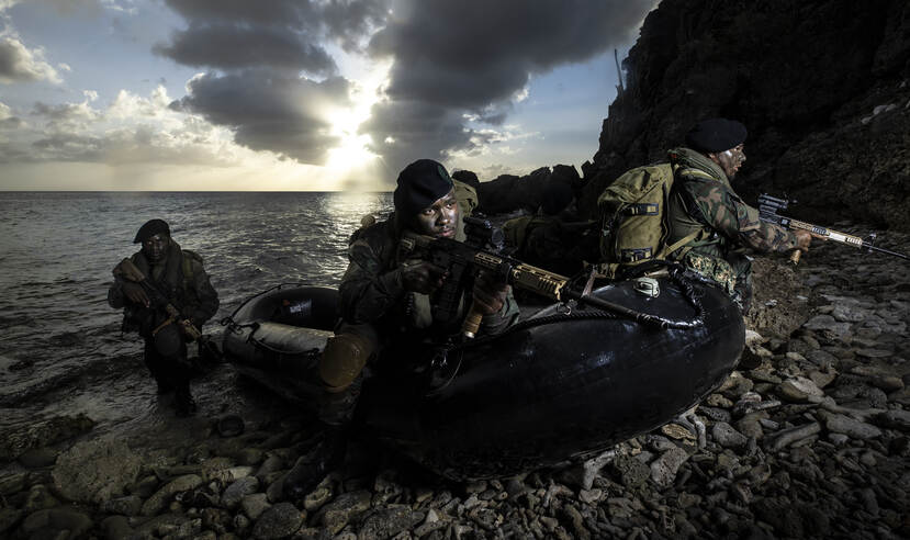 3 militairen met geweren komen in een rubber boot aan land.