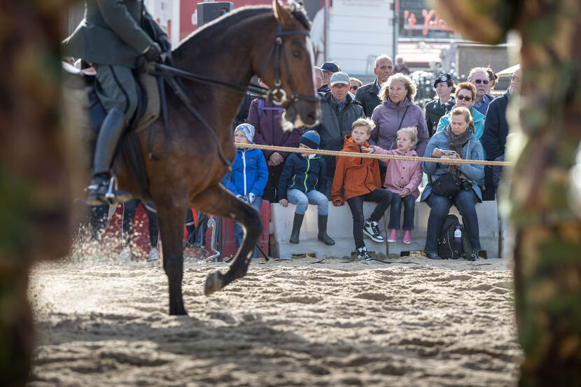 Publiek kijkt hoe militairen te paard oefenen voor Prinsjesdag op het strand.