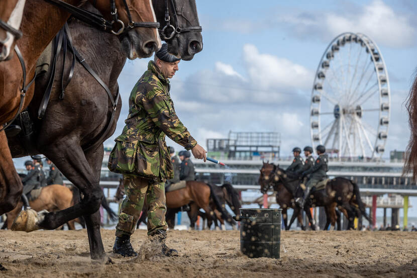 Een militair steekt een rookbom tijdens het oefenen met paarden op het strand.