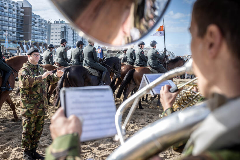 Militairen spelen muziek tijdens het oefenen met paarden op het strand.