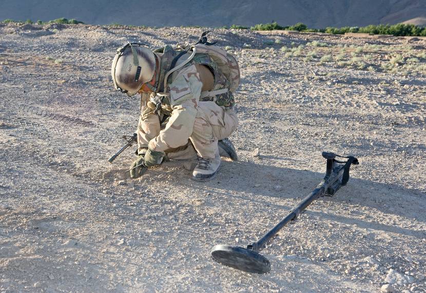 Militair zoekt tijdens een voetpatrouille in Uruzgan naar eventueel verstopte bermbommen.