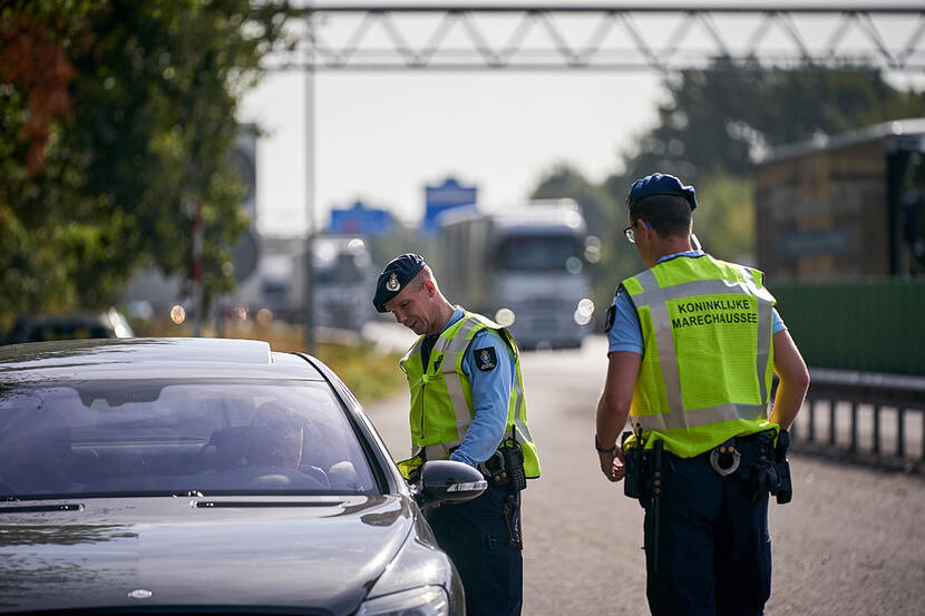 2 marechaussees controleren reisdocumenten van een chauffeur van een auto.