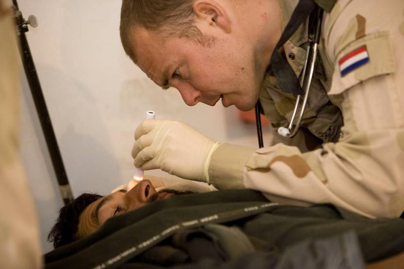 Een militair verpleegkundige bekijkt het oog van een patient.