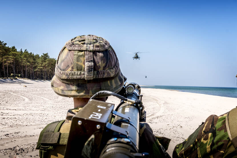 Militair staat op strand en richt stinger-luchtdoelraker op helikopter.