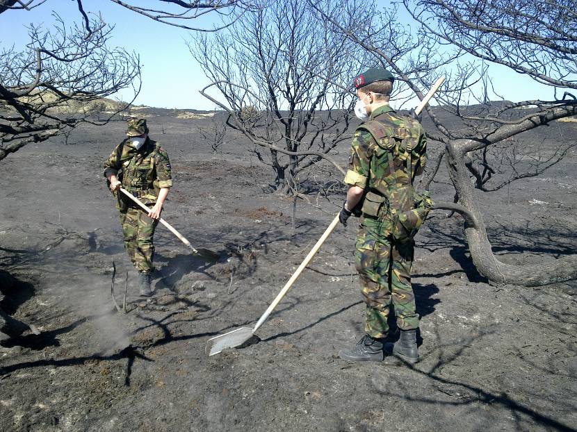 Militairen Korps Nationale Reserve met schoppen helpen natuurbrand in duinen doven.