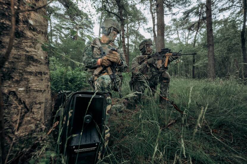 2 gecamoufleerde militairen hurkend in een bos ieder met een Colt-geweer.