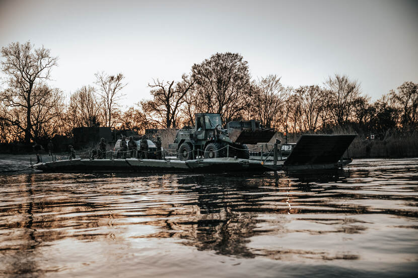 Een pontonbrug (dit is een tijdelijke brug) over het water met op de brug meerdere militairen en een voertuig.