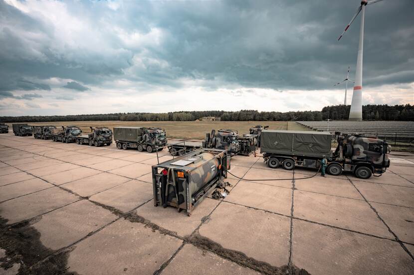 Militaire vrachtwagens staan achter elkaar in een rij om afgetankt te worden.