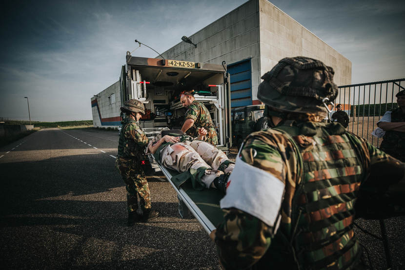Militair geneeskundigen voeren een oefenpatiënt af per ziekenauto.