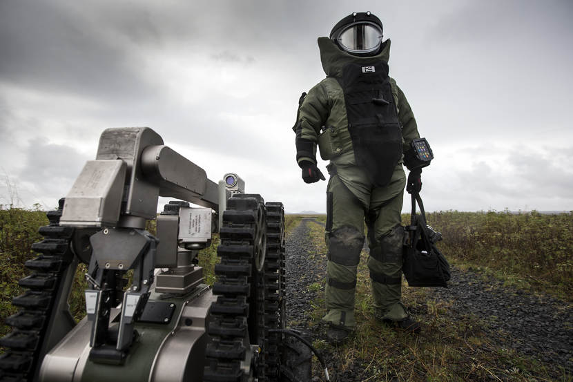 Een explosievenruimer van de EOD in het zware bommenpak en de explosievenrobot Telemax staan op het punt een gebouw binnen te gaan om een geïmproviseerd explosief te ruimen tijdens een oefening in IJsland (2016).