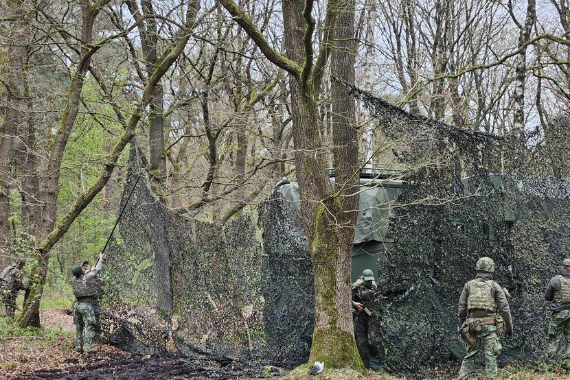 Militairen plaatsen een camouflagenet over boomtoppen.