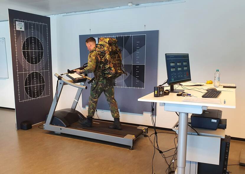 Militair loopt in een onderzoeksruimte met bepakking en nepwapen op een loopband.