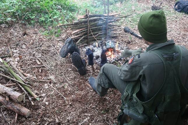 Een militair maakt een vuurtje in het bos.