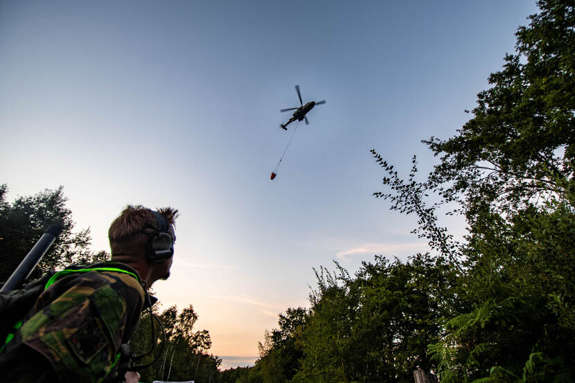 Een militair kijkt omhoog naar een helikopter met een bambi bucket.