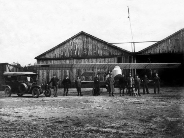 Een Farman HF-20 met personeel van de Luchtvaartafdeeling voor de houten hangars op de Molenheide in 1914.
