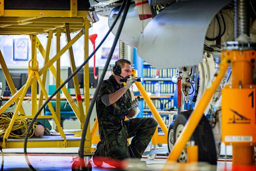 Militair schijnt met zaklamp op de wielophanging van een vliegtuig.