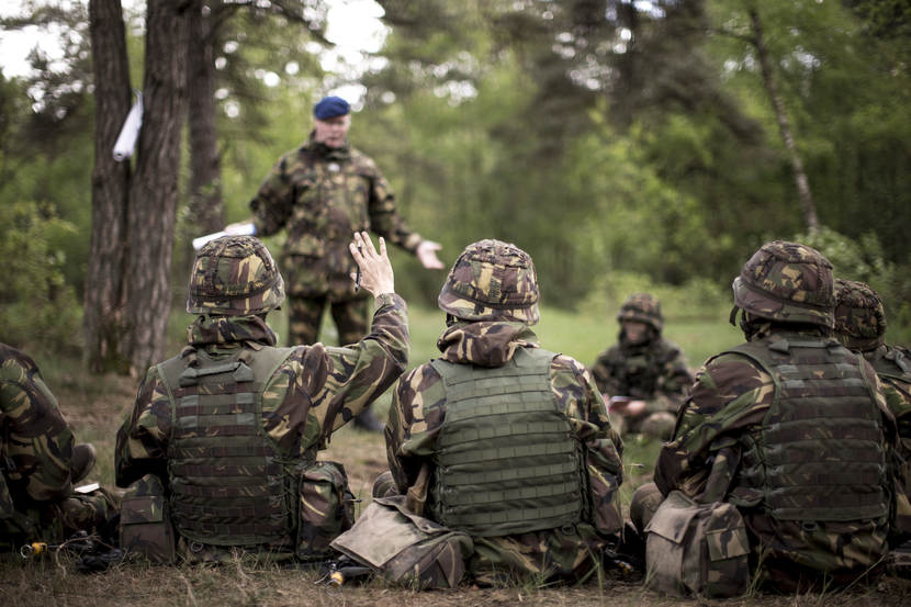 Leerlingen in camouflagepak luisteren naar docent.