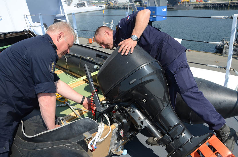 2 marinemannen bekijken een buitenboordmotor van een RHIB.