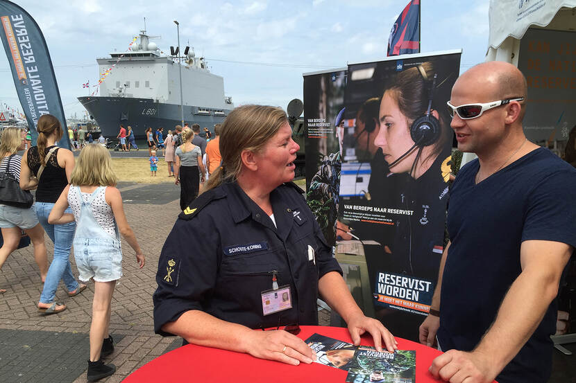 Marinevrouw in gesprek met een burger, tijdens de Marinedagen in de haven in Den Helder. Op de achtergrond een marineschip.